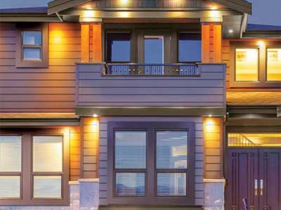 Front view of a mid-class, two-story home at dusk with its exterior lights on, showcasing light blue Royal siding