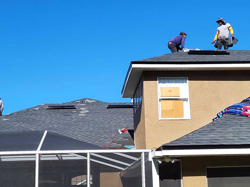 Two Total Roofing Solutions & Construction workers installing new GAF gray shingles on a large residential roof