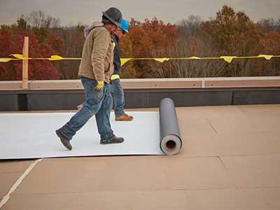 Two workers unrolling a TPO roofing sheet