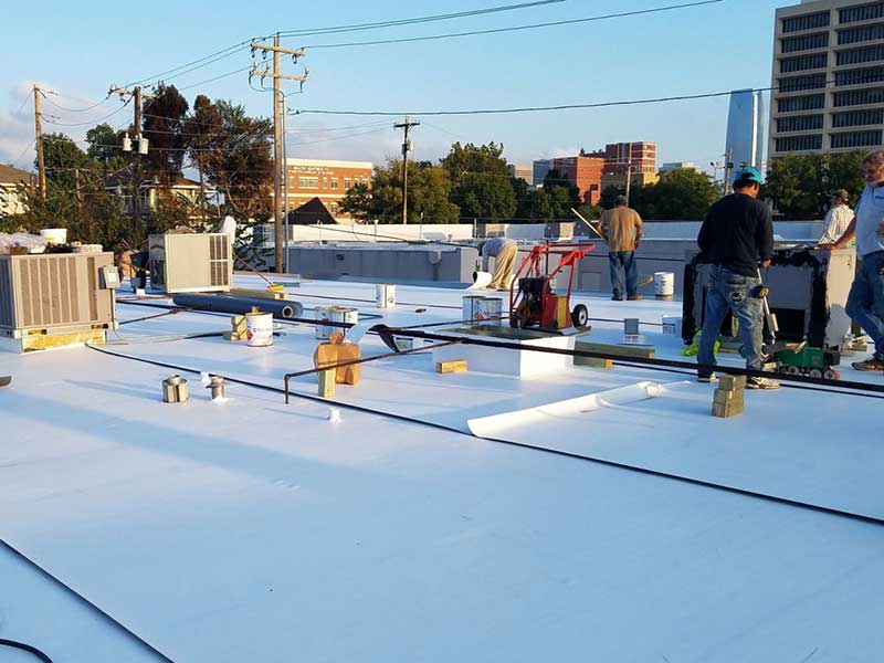 Total Roofing Solutions & Construction workers finishing up a job involving the installation of a new white TPO system on a large, flat commercial roof