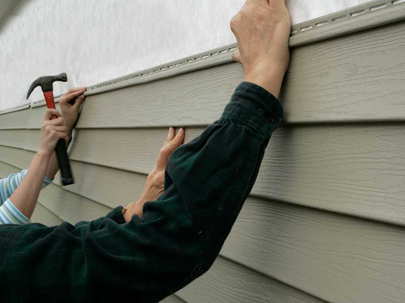Close up of two workers installing green vinyl siding on a home with a hammer